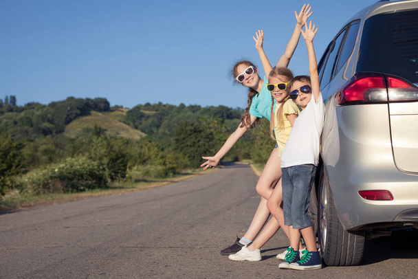 Onnellinen veli ja hänen kaksi siskoaan seisovat auton lähellä päivällä. Lapset pitävät hauskaa ulkona. Perheen käsite on valmis matkustamiseen
. - Valokuva, kuva