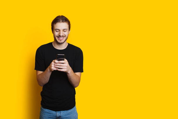 Μακρυμάλλης καυκάσιος άνδρας συνομιλεί με κάποιον στο τηλέφωνο χαμογελά σε ένα κίτρινο φόντο με ελεύθερο χώρο - Φωτογραφία, εικόνα