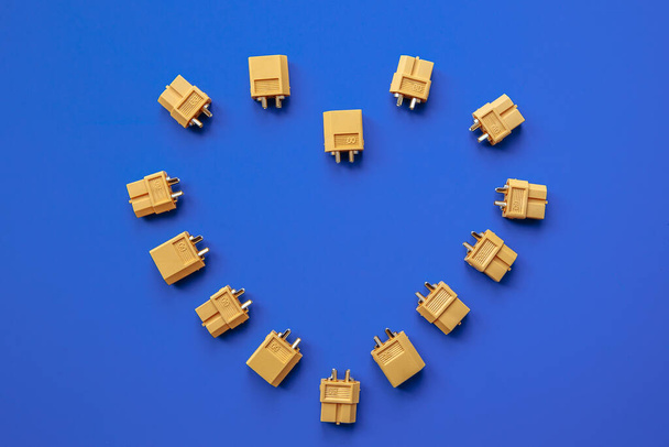 Heart made of yellow XT-60 connectors for power supply on a blue background. The heart of an electronic engineer. - Fotoğraf, Görsel