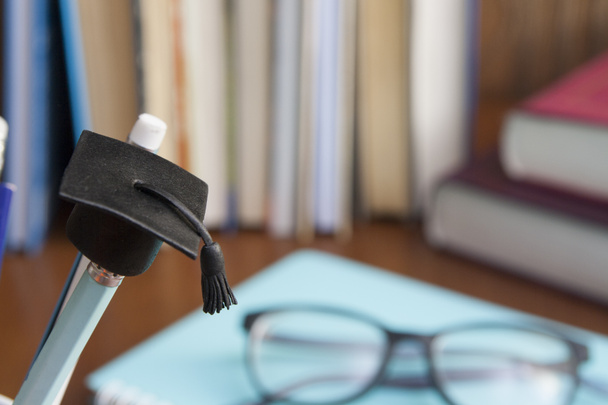 Sombrero de graduado en un lápiz en el fondo de libros y gafas. Concepto de educación
 - Foto, Imagen