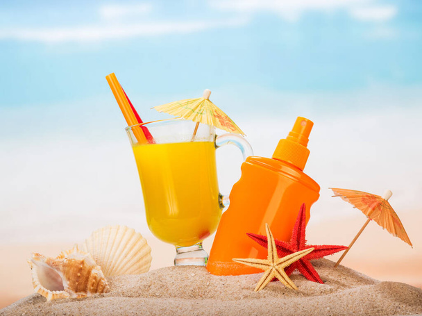 Szklanka soku, filtra przeciwsłonecznego, parasole, rozgwiazdy i muszle w piasku nad morzem. - Zdjęcie, obraz
