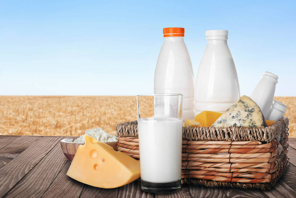 Diferentes productos lácteos sobre mesa de madera en campo de trigo
  - Foto, Imagen