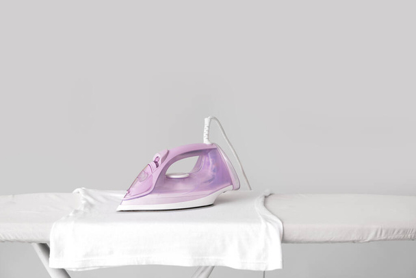 Electric iron with clothes on board against grey background - Foto, Bild