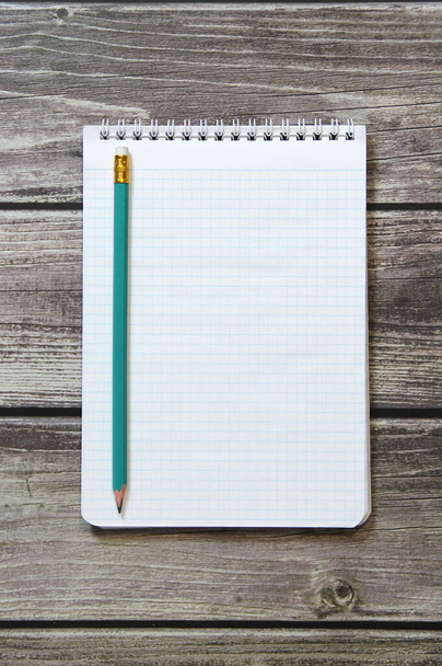 Notepad with a blank white sheet in a checker paper with simple graphite pencil lies on the background of wooden boards - Photo, image