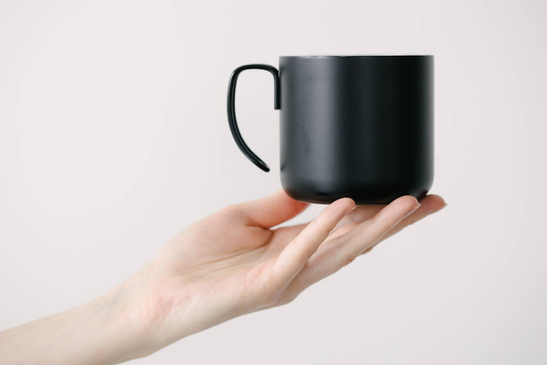 Black metal cup for tea and coffee in woman hand over white background - Photo, Image