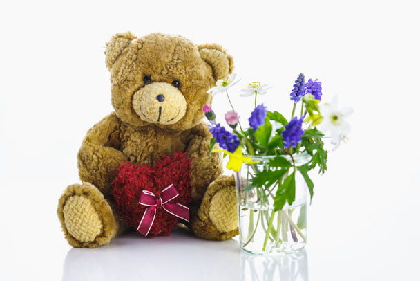 Teddy bear against a white background and flowers in a vase. Spring. - 写真・画像