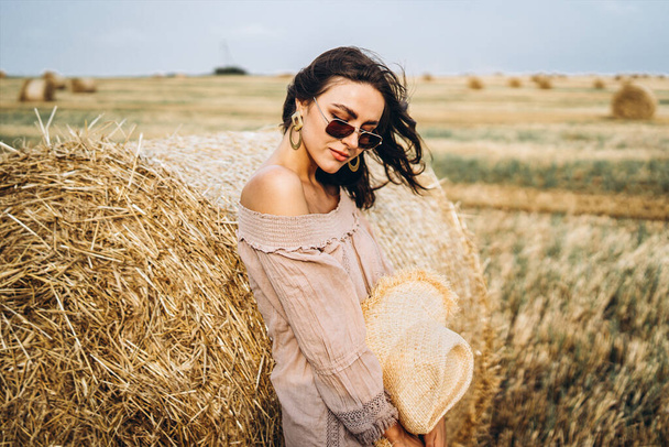 Smiling woman in sunglasses with bare shoulders on a background of wheat field and bales of hay. - Φωτογραφία, εικόνα