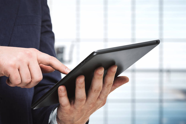 Ο άνθρωπος πατάει στην οθόνη ενός ψηφιακού tablet στην ηλιόλουστη αίθουσα συνεδριάσεων, κοντά. Έννοια ηλεκτρονικής τεχνολογίας - Φωτογραφία, εικόνα