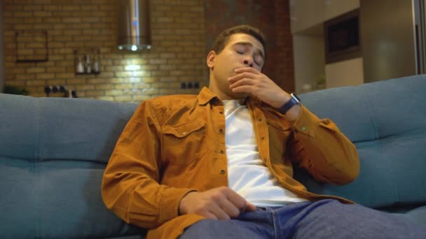 Overworked young man watching tv until late night, falling asleep on couch home - Video