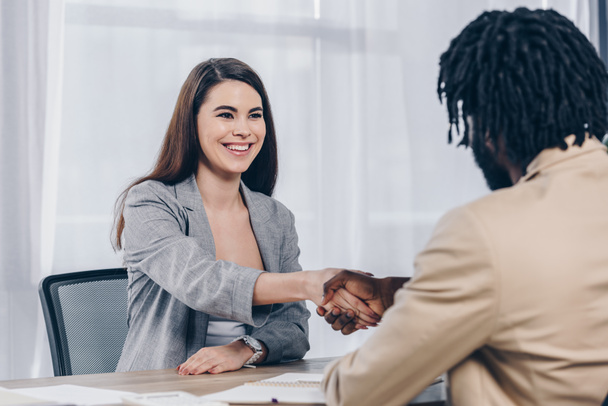 Enfoque selectivo del empleado sonriendo y estrechando la mano con el reclutador afroamericano en la entrevista de trabajo en la oficina
 - Foto, Imagen
