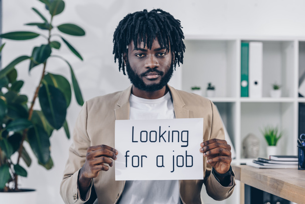African american employee showing placard with looking for a job lettering in office - Foto, immagini