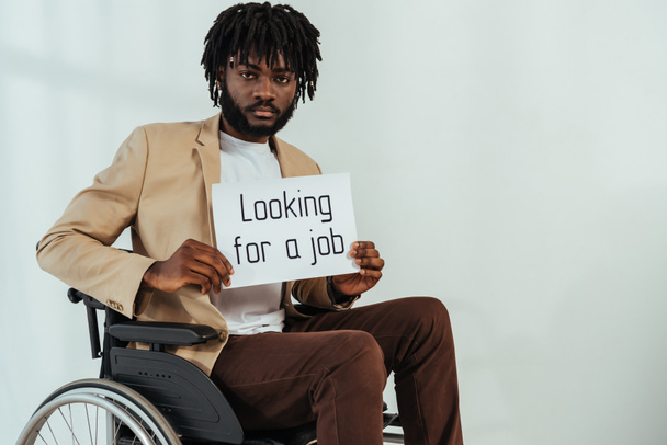 Behinderter afrikanisch-amerikanischer Mann mit Plakat mit Stellensuche Schriftzug auf Rollstuhl auf weißem Grund  - Foto, Bild