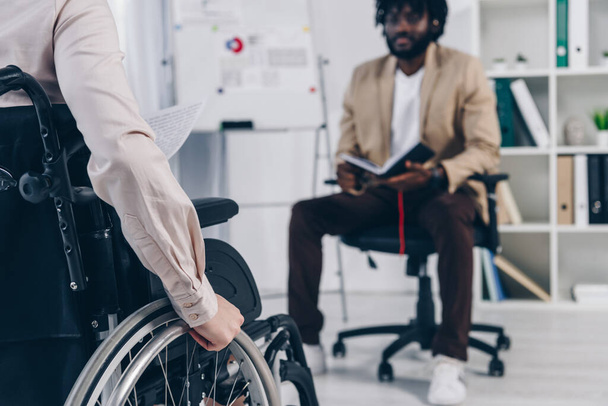 Cropped view of disabled recruiter on wheelchair and african american employee with notebook in office - Фото, изображение