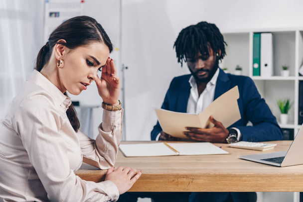Stressed employee and african american recruiter with folder at table in office - Foto, afbeelding
