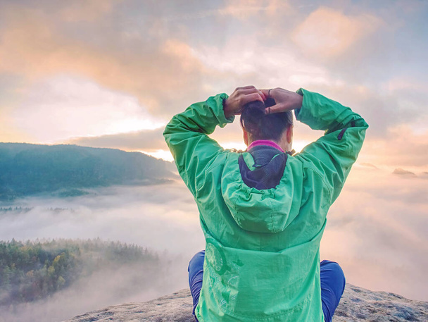 La giovane donna si siede sulla cima di una montagna per festeggiare il giorno. Giovane escursionista seduta in giacca a vento verde blu con zaino rosso su scogliera affilata
 - Foto, immagini