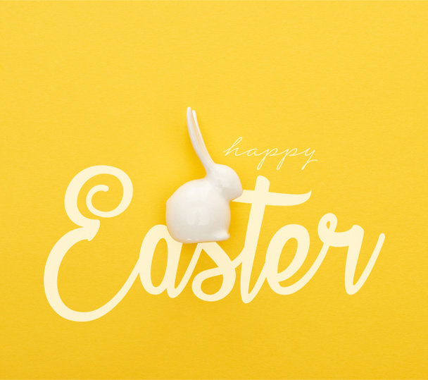 vrchní pohled na bílé velikonoční zajíček na barevném žlutém pozadí se šťastnou velikonoční ilustrací - Fotografie, Obrázek