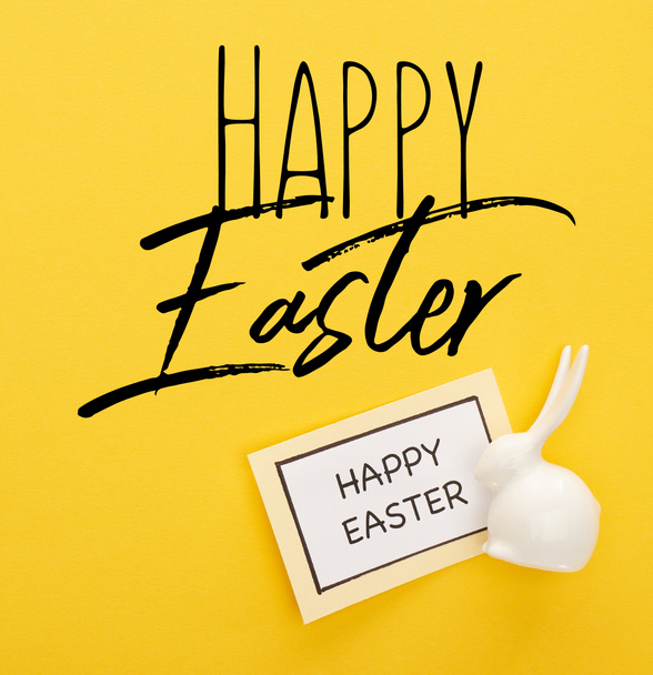 top view of greeting card with happy Easter lettering near Easter white bunny on yellow colorful background - Foto, imagen