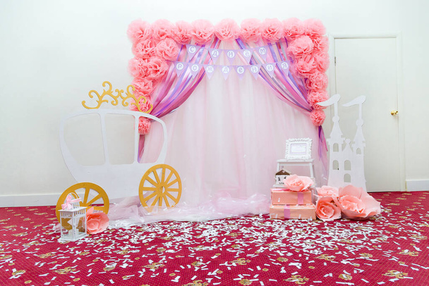 Beautiful pink photo zone for one year old baby girl with paper flowers, wrapped present boxes, wooden castle and princess carriage or cab. Inscription on flags in Russian reads Happy Birthday. - Photo, Image