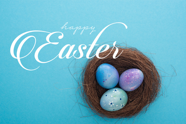 Vue du dessus du nid avec des œufs de Pâques violets sur fond bleu avec une heureuse illustration de Pâques
 - Photo, image