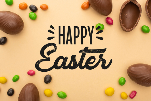 Top view of chocolate eggs and tasty sweets on beige background with happy Easter illustration - Photo, Image