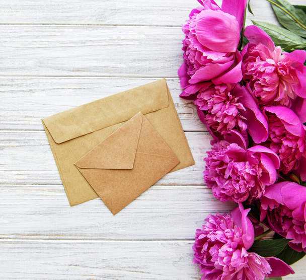 Bruiloft uitnodiging en envelop met roze pioenrozen op een oude witte houten achtergrond - Foto, afbeelding