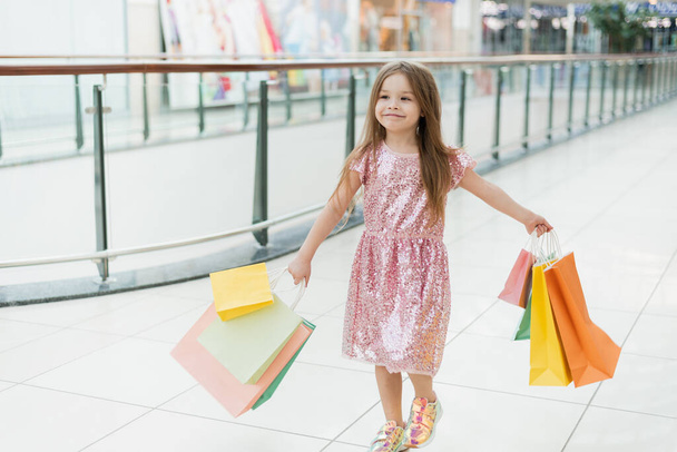 Vrolijk kleuter meisje dat met boodschappentassen loopt. Mooie glimlachende kleine meid met boodschappentassen poserend in de winkel. Het concept van winkelen in winkels. - Foto, afbeelding