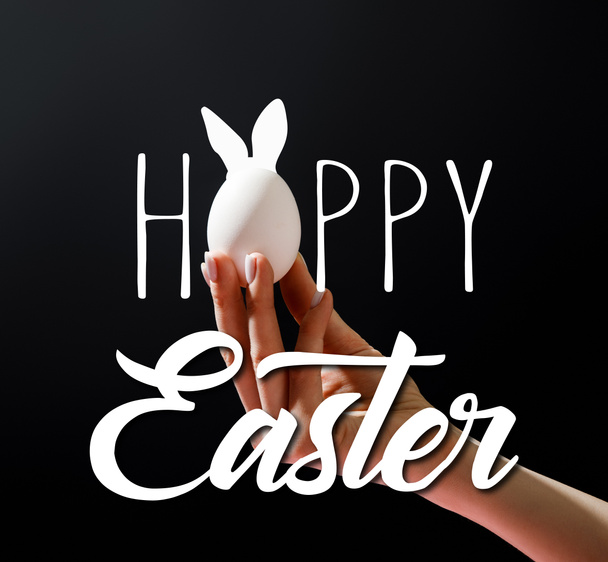 Cropped view of woman holding chicken egg isolated on black with happy Easter illustration - Photo, Image