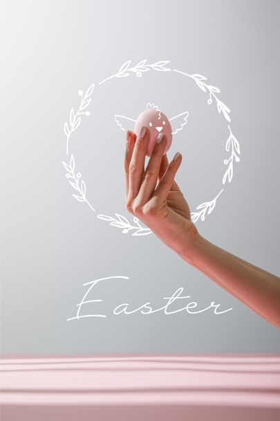 Cropped view of woman holding chicken egg isolated on grey background with Easter illustration - Фото, изображение