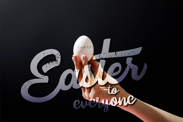 Cropped view of woman holding chicken egg isolated on black with happy Easter to everyone illustration - Photo, Image