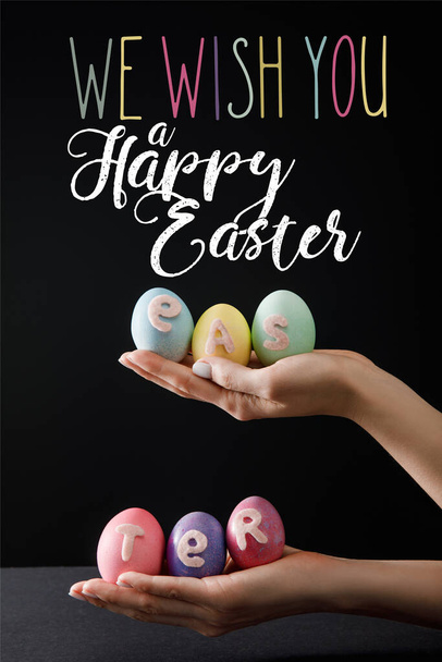 Selective focus of Easter eggs on wooden board on black with we wish you a happy Easter illustration - Foto, immagini