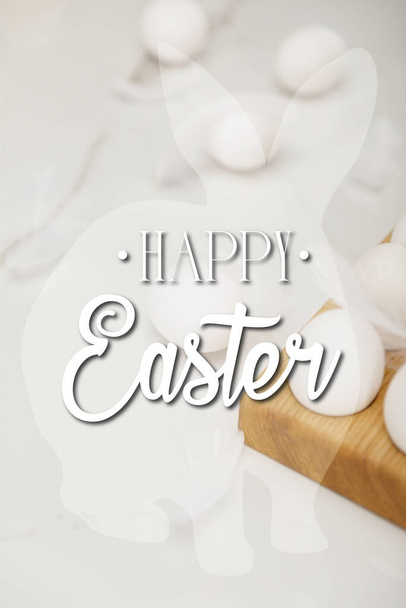 Selective focus of eggs on wooden egg tray and feathers on white background with happy Easter illustration - Photo, image