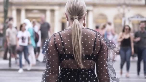 Rear view of a pretty woman in black transparent dress crossing the street near the crowd of people. Action. Sexy blond plus size model walking in a big city. - Video