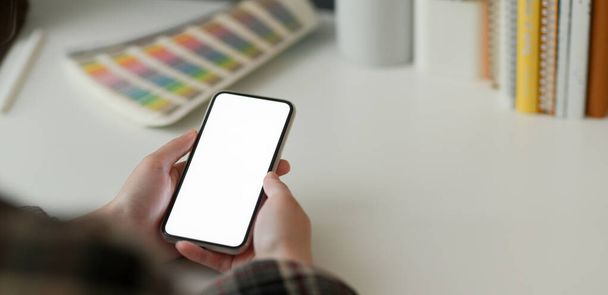 Обрезанный снимок женщины-дизайнера с помощью макета смартфона во время работы с дизайнерскими принадлежностями на белом столе
 - Фото, изображение