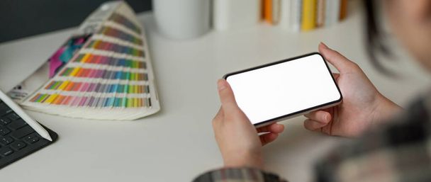 Обрізаний знімок жіночого дизайнера, який тримає горизонтальний макет смартфона під час роботи з дизайнерськими приладдям на білому столі
 - Фото, зображення