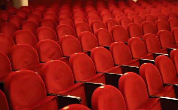Klasyczne rzędy pustych, czerwonych miejsc w teatrze. Sala bez gości. Płytka głębia ostrości - Zdjęcie, obraz