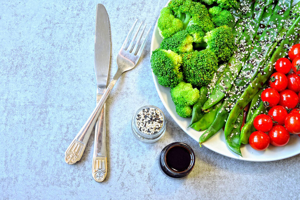 Gesundes Essen auf dem Teller. Grüne Bohnen, Brokkoli, Kirschtomaten. Nützlicher Salat aus grünem Gemüse mit gebackenen Kirschtomaten und Sesam. Produkte für die Gesundheit. - Foto, Bild
