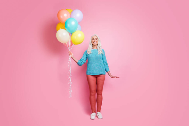 Full size photo of pretty charming old woman babysitter prepare birthday for her grandchildren hold many air baloons wear jumper gumshoes isolated over pastel color background - Фото, зображення
