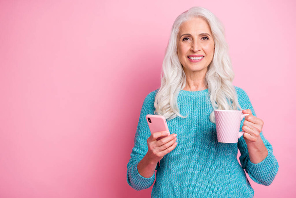 Charming old woman modern granny use smart phone texting typing chatting family read social network news hold beverage mug wear casual style blue sweater isolated pastel color background - Fotografie, Obrázek