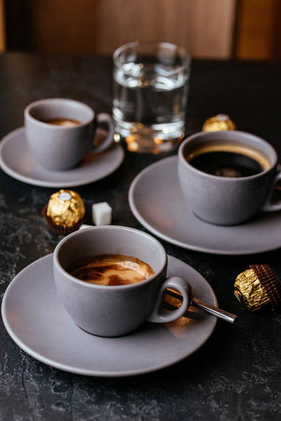 americano coffee cups with chocolate candies on gray background - Photo, Image