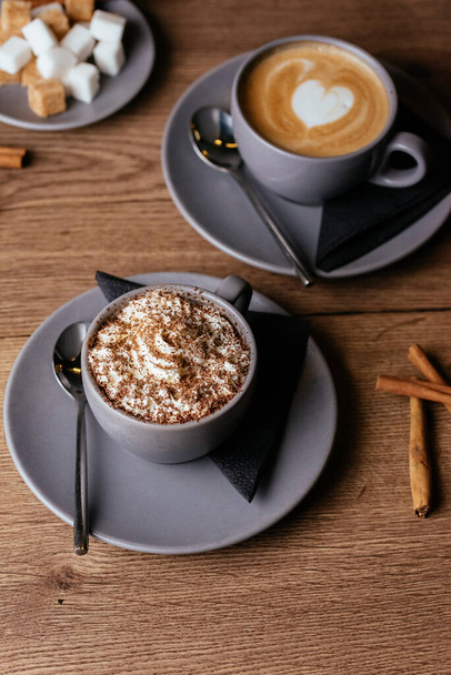 κούπες καφέ με σαντιγί και φέτες ζάχαρης σε ξύλινο φόντο - Φωτογραφία, εικόνα