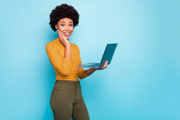 Profile photo of pretty dark skin curly lady hold notebook hands reading good news modern technology user wear yellow striped jumper isolated blue color background - Φωτογραφία, εικόνα