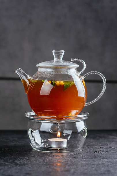 thee glazen pot met duindoorn en groene thee bladeren met kaars op tafel achtergrond - Foto, afbeelding