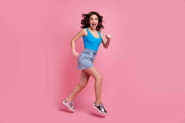Full body profile photo of pretty crazy lady jump high rushing shopping center sale season wear blue tank-top denim short skirt shiny footwear isolated pink color background - Photo, image