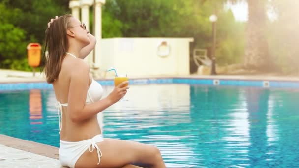 Vrouw met sinaasappelsap ontspannend bij het zwembad. - Video