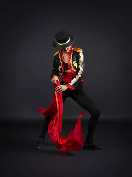 Plastic girl gracefully dancing in a stage costume stylized as a bullfighter. Studio shooting on a dark background. - Photo, image