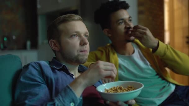 Two male friends watching soccer match on tv, celebrating goal, chewing snacks - Footage, Video