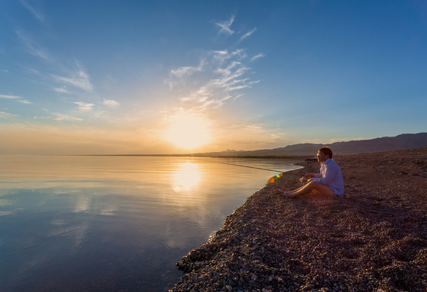 Фішер людина з силует вудкою на березі моря, на заході сонця - Фото, зображення