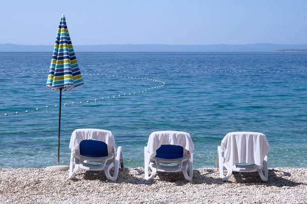 Chaises con toallas blancas y sombrilla de playa para relajarse en el balneario. Vacaciones de verano y viajes por la costa. Servicio de pago en playas confortables
. - Foto, imagen