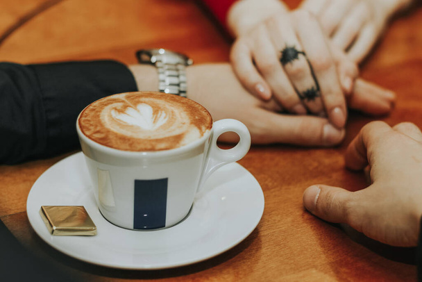 Hands of a man hold hands of a girl around a cup of coffee in the foreground on the table. Romantic atmosphere. A pair of hands. Close up - Foto, Imagen