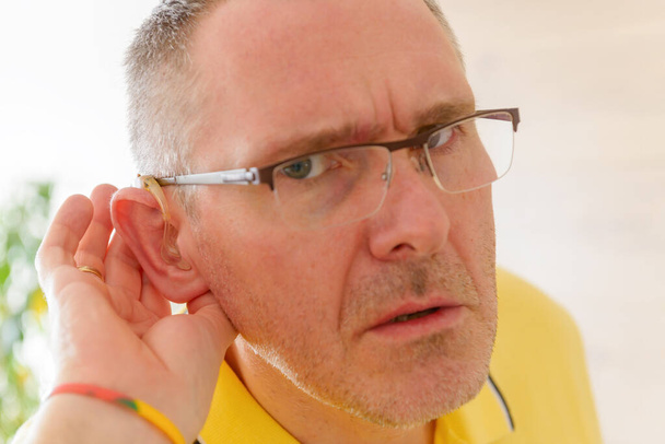 Чоловік у глухій допомозі в вусі намагається щось почути
 - Фото, зображення